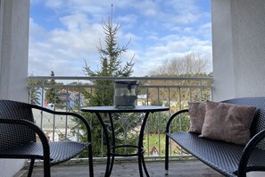 Ein Balkon mit zwei Korbstühlen, einem kleinen runden Tisch und einem Sitzkissen.