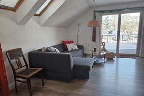 Sala de estar no estilo loft com pé direito alto, claraboia, sofá cinza, cadeira de madeira e mesa de vidro.