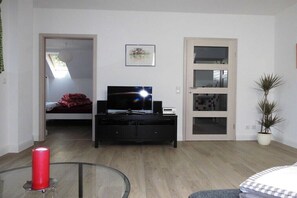 Uma sala de estar moderna com TV, uma mesa de vidro, uma vela vermelha e um vaso de planta.