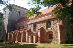 Ein historisches Steinhaus mit rotem Ziegeldach, Bogenfenstern und einem überdachten Gang.