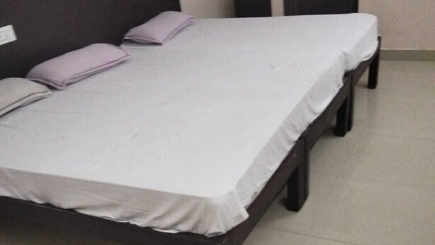 Una cama individual con colchón blanco y estructura de madera oscura, una mesita de noche pequeña y un aparador de pared.