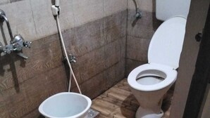Un baño con piso de madera, inodoro y un balde.