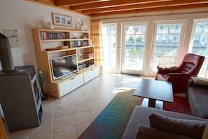 Ein Wohnzimmer mit Fernseher, Bücherregal, rotem Sessel und Blick durch Glastüren.