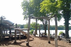 Ein Spielplatz mit Holzgerüsten und Blick auf einen See.