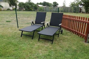 Zwei Gartenliegen mit Metallgestellen und dunklen Stoffsitzen auf einer Rasenfläche neben einem Holzzaun.