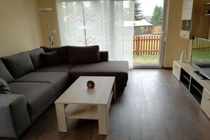 Ein Wohnzimmer mit einem Ecksofa, einem Couchtisch, einer TV-Bank und einer Schiebetür zu einem Hinterhof.