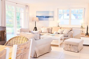 Ein helles Wohnzimmer mit einer Sofagarnitur, einem Couchtisch, einem Kamin und großen Fenstern.
