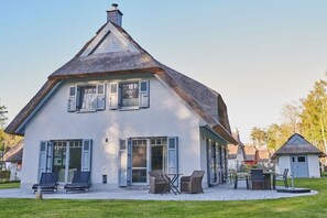 Ein Haus mit einem steilen Satteldach, großen Fenstern mit Fensterläden und einer Terrasse mit Gartenmöbeln.