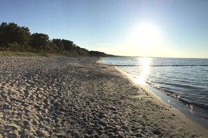 Ein Strand mit blauem Himmel, ruhigem Wasser und einer fernen Küstenlinie.