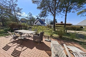 Eine Terrasse mit Tisch und Stühlen, umgeben von Bäumen und einem Haus im Hintergrund.