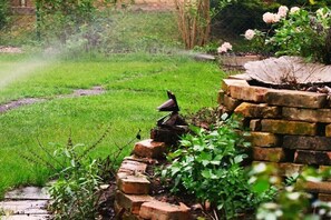 Ein Garten mit Vogeltränke, Mauerwerk und blühenden Pflanzen.
