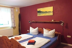 Ein Zimmer mit zwei Betten, einem fensterbelaubten Fenster, einem Heizkörper und einem Bild an der Wand.
