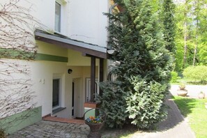 Ein Gebäude mit einer überdachten Veranda, einem großen Nadelbaum und einem Weg zum Eingang.
