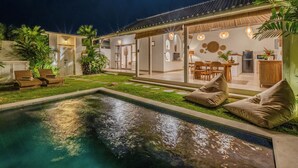 Ein Poolbereich mit Liegestühlen, ein Essbereich mit Tisch und Stühlen sowie eine durchgehende Tür erkennbare Küche.