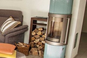 Ein Zimmer mit einem grauen Sofa, einem gestreiften Kissen, einem Holzkorb und einem Kaminofen.
