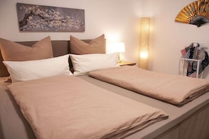Ein Hotelzimmer mit einem Bett, Kissen, einer Nachttischlampe, einem Wandventilator und einem Gemälde.