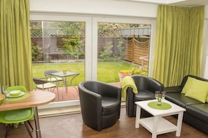 Ein Zimmer mit einer Couch, Sesseln, einem Tisch und Blick auf einen Garten durch große Fenster.
