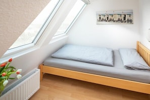 Ein kleines Zimmer mit einem Einzelbett, einer schrägen Decke, einem Heizkörper und einem Fenster.
