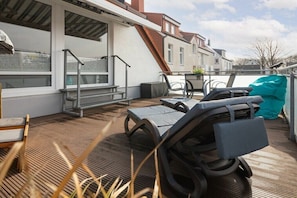 Eine Dachterrasse mit Liegestühlen, einem Tisch und einem überdachten Bereich.
