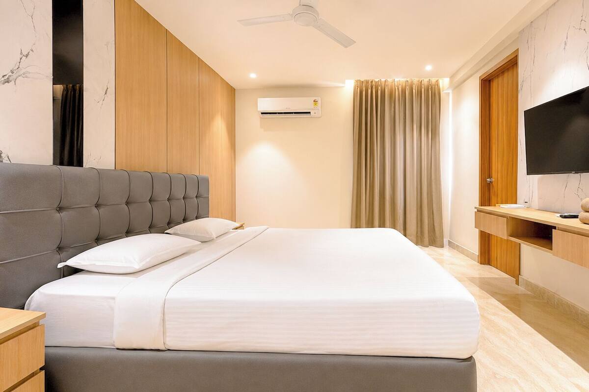 Habitación de hotel moderna con una cama grande, televisión, mueble de madera y ventilador de techo.