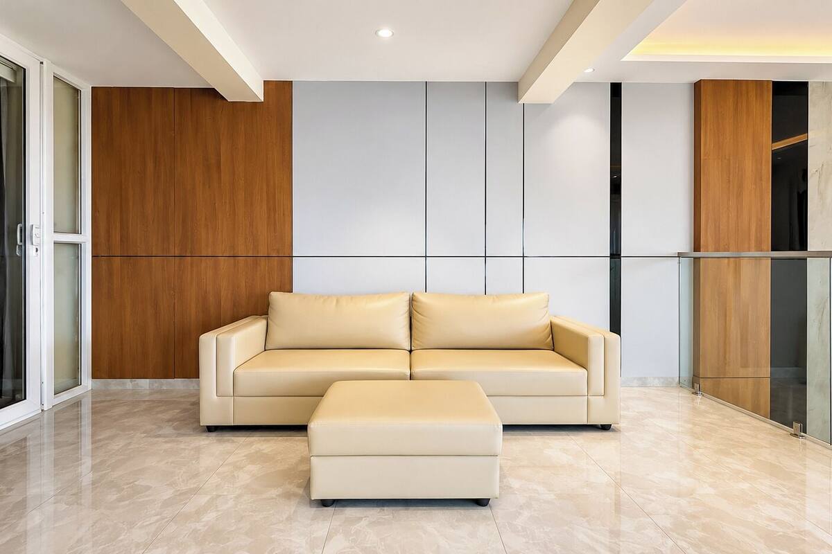 Una sala de estar moderna con un sofá y reposapiés color beige, paneles de madera y un separador de vidrio.