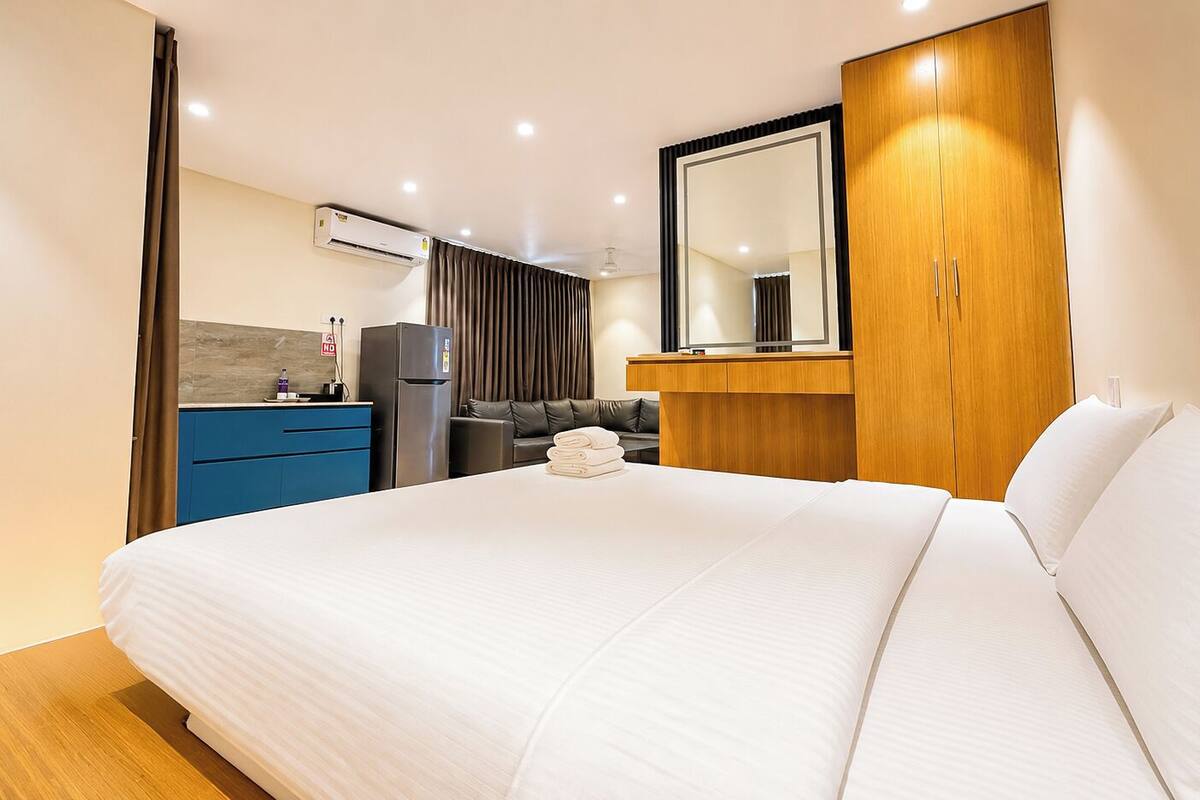 Habitación de hotel con una cama grande, un armario de madera, un espejo, un escritorio con una silla y una kitchenette.