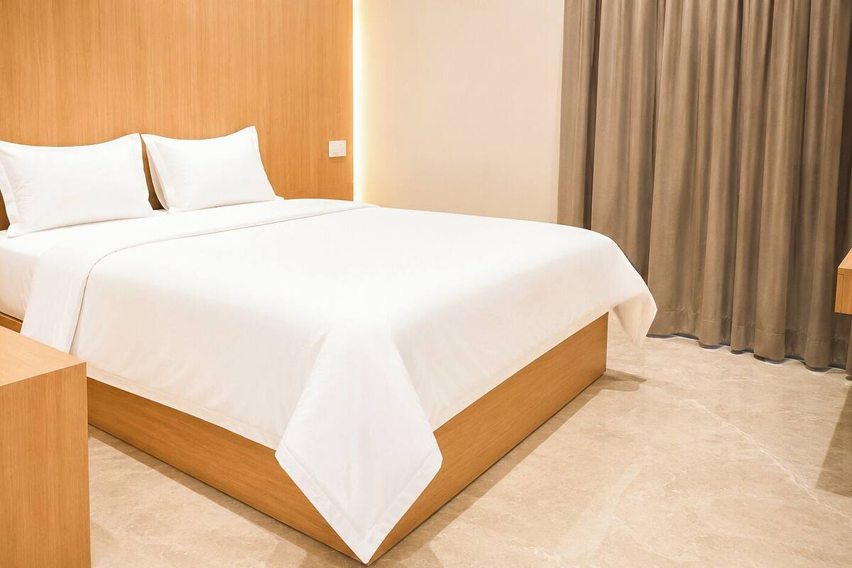 Una cama bien hecha con sábanas blancas, cabecera y mesita de noche de madera.