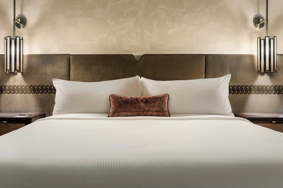 Habitación de hotel con una cama grande, dos mesitas de noche, cabecero e iluminación en la pared.