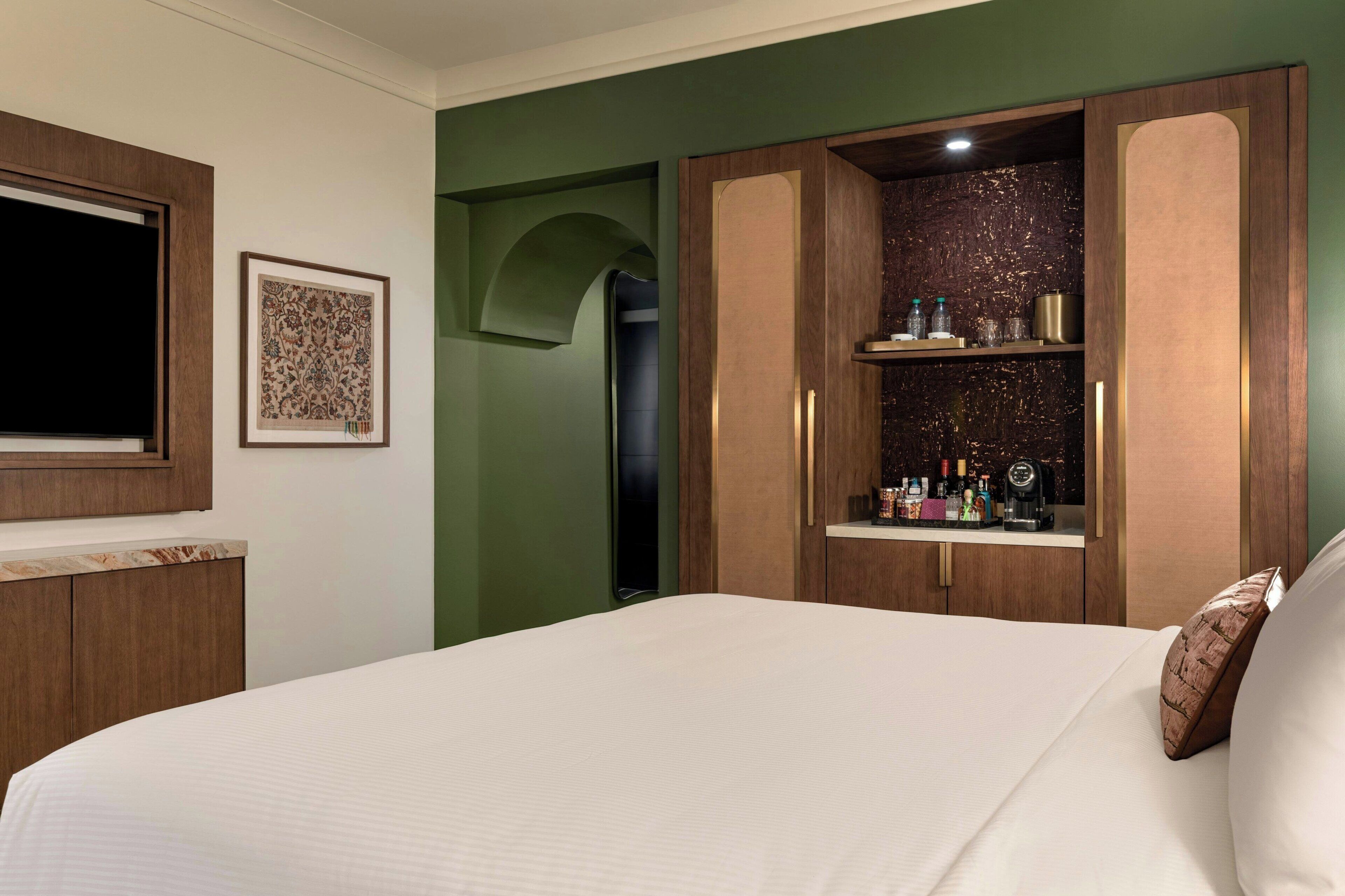 A hotel room with a bed, a wardrobe, a framed picture, and a shelf with toiletries.