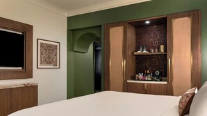 Habitación de hotel con cama, armario, un cuadro enmarcado y repisas con artículos de aseo.