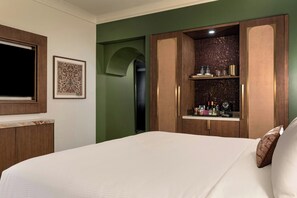 A hotel room with a bed, a wardrobe, a framed picture, and a shelf with toiletries.