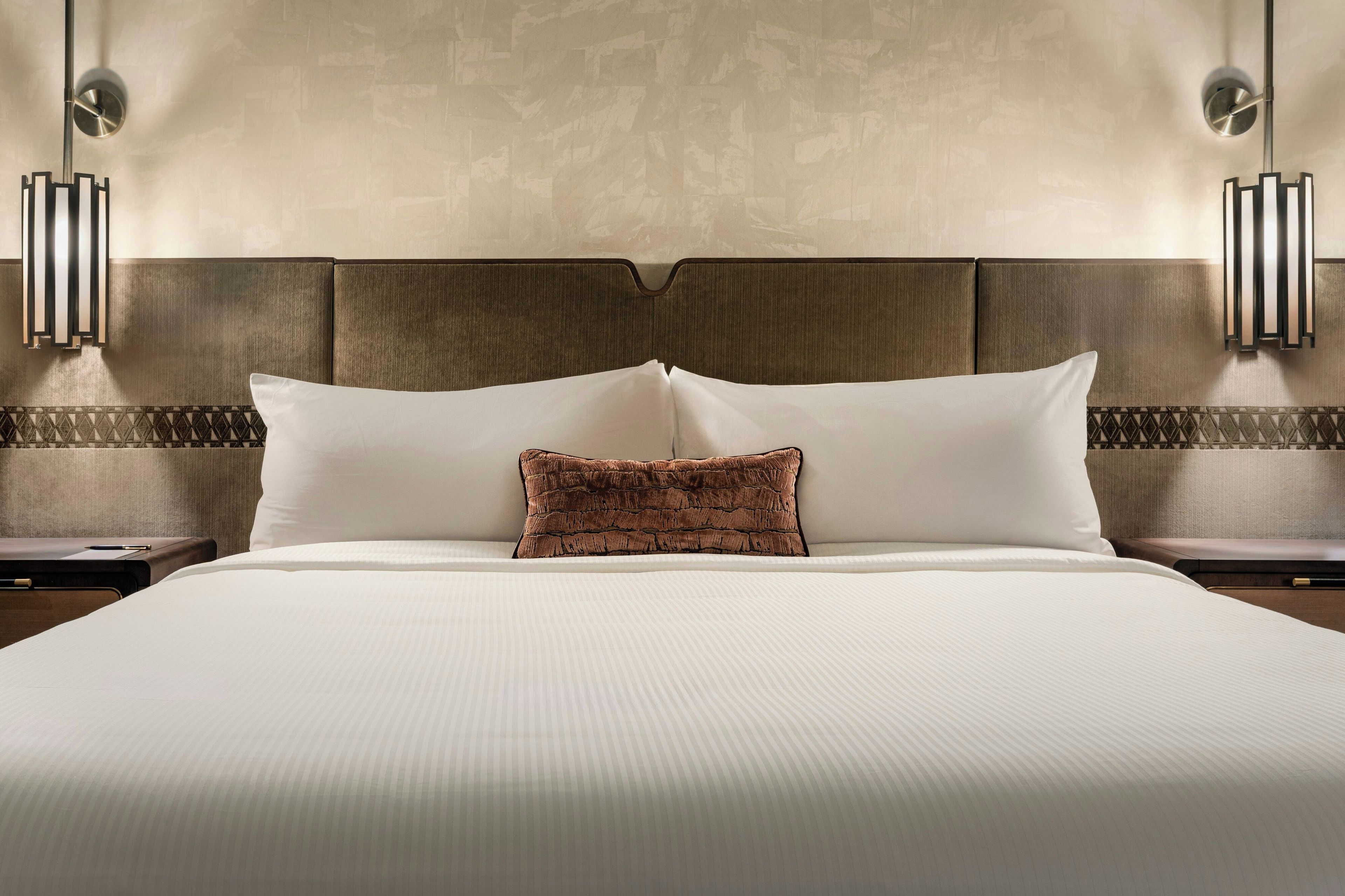 Habitación de hotel con una cama grande, dos mesitas de noche, cabecero e iluminación en la pared.
