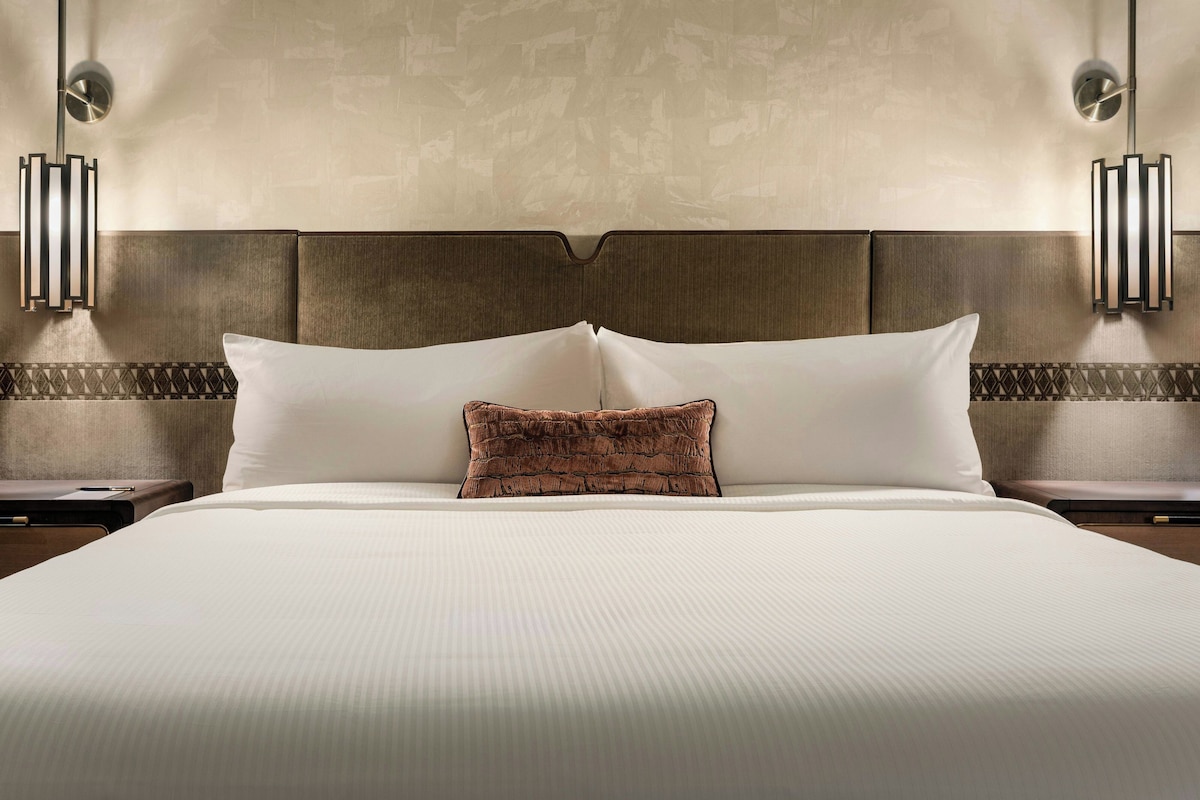 Une chambre d’hôtel avec un grand lit, deux tables de chevet, une tête de lit et des lampes fixées au mur.