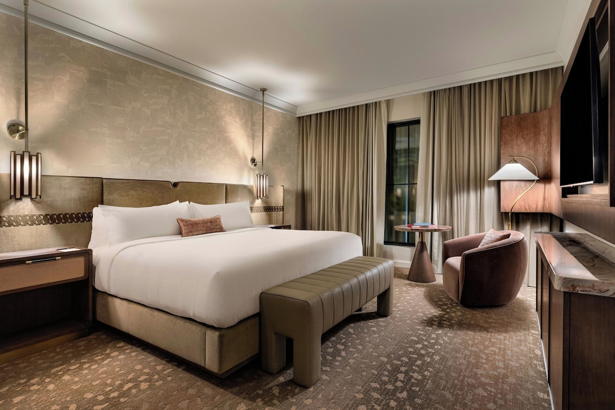 Une chambre d’hôtel avec un grand lit, une banquette, un bureau, une chaise, une télévision et une petite table.