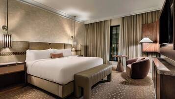 A hotel room with a large bed, a bench, a desk, a chair, a TV, and a small table.