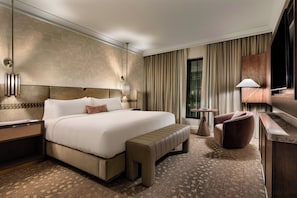 Une chambre d’hôtel avec un grand lit, une banquette, un bureau, une chaise, une télévision et une petite table.