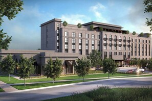 A modern hotel with a flat roof, multiple balconies, and a landscaped front yard.