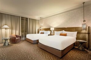 A hotel room with two beds, a sitting area, and a large window with curtains.