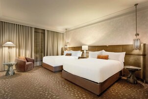 Habitación de hotel con dos camas, una zona de estar y un ventanal grande con cortinas.