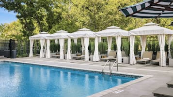 A swimming pool with lounge chairs and umbrellas, surrounded by a fence and trees.