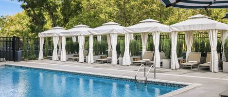 A swimming pool with lounge chairs and umbrellas, surrounded by a fence and trees.
