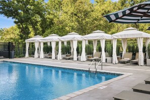 A swimming pool with lounge chairs and umbrellas, surrounded by a fence and trees.