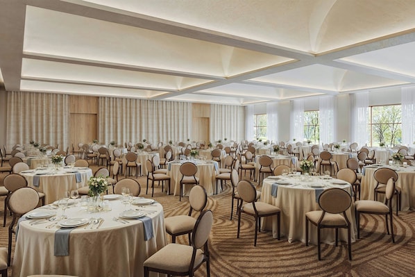 A large banquet hall with round tables, chairs, and a carpeted floor.