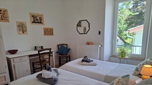 Une chambre avec deux lits, un bureau, une chaise, un radiateur et une fenêtre donnant sur un espace verdoyant.