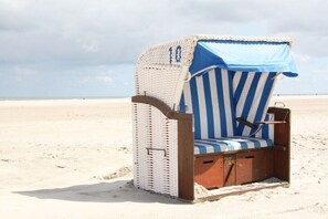 Ein Liegestuhl mit gestreifter Auflage und blauer Hülle, platziert an einem Sandstrand.