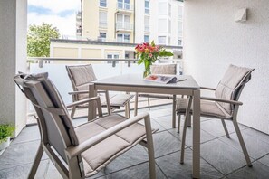 A balcony with a table and chairs, a vase with flowers, and a building in the background. - Düsseldorfer Hof A1 - first class living (Norderney)