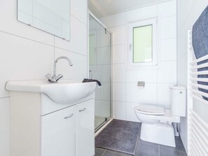 Ein modernes Badezimmer mit einem weißen Waschbecken, einer Duschkabine aus Glas, einer Toilette und einem Handtuchhalter.