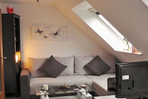 Ein modernes Wohnzimmer mit einer Couch, einem Glastisch und einem Flachbildfernseher.