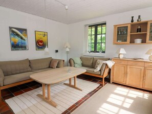 Ein Wohnzimmer mit einer Couch, einem Holztisch, einem Schrank und einem Fenster mit Blick auf Grünflächen.