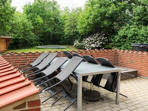 Eine Terrasse im Freien mit einer Backsteinmauer, einem Tisch mit Stühlen und einem Garten mit Bäumen und Blumen.